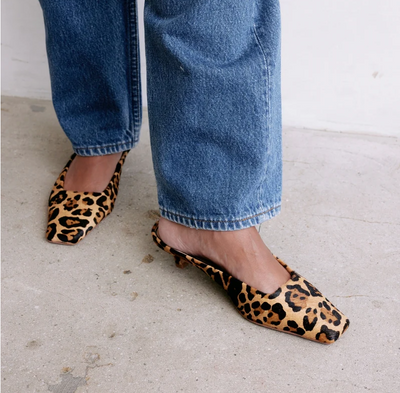 Leopard print cowhide kitten heel mules on model's feet.