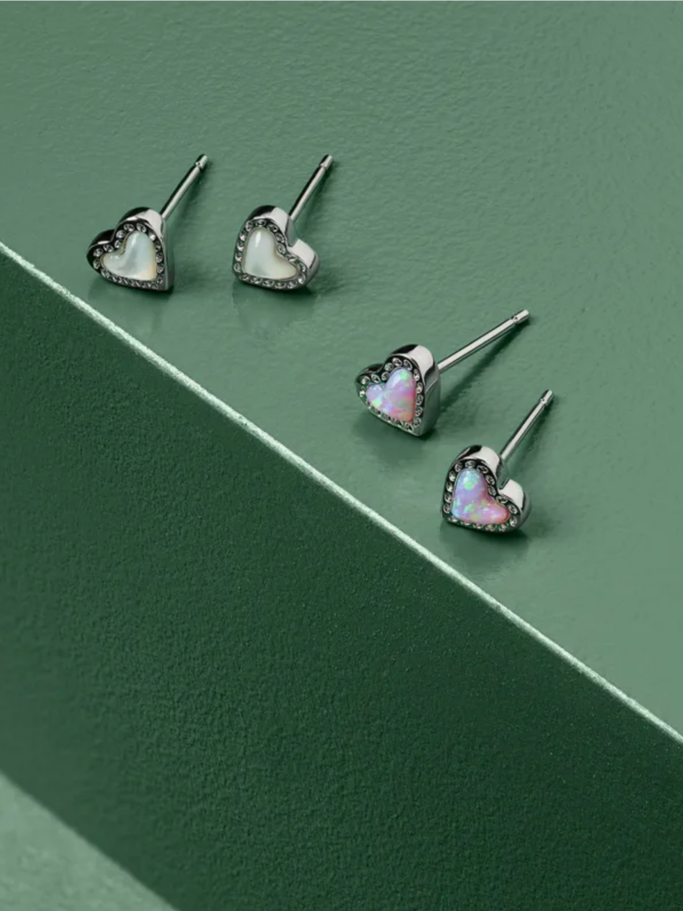 Silver framed ivory mother of pearl and pink kyocera opal heart studs on green box background.