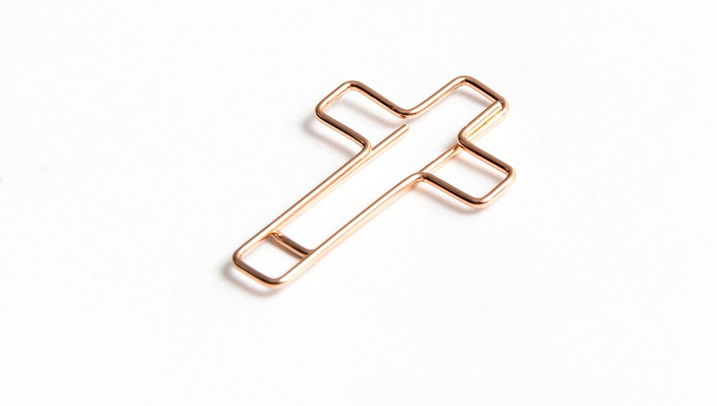 Cross shaped rose gold paper clip, sideways.