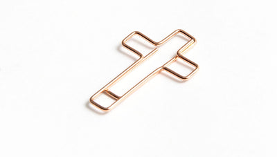 Cross shaped rose gold paper clip, sideways.