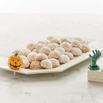 Orange pumpkin with a green stem and black and gold trimmed jack o'lantern face mini on display with a bread tray of cookies