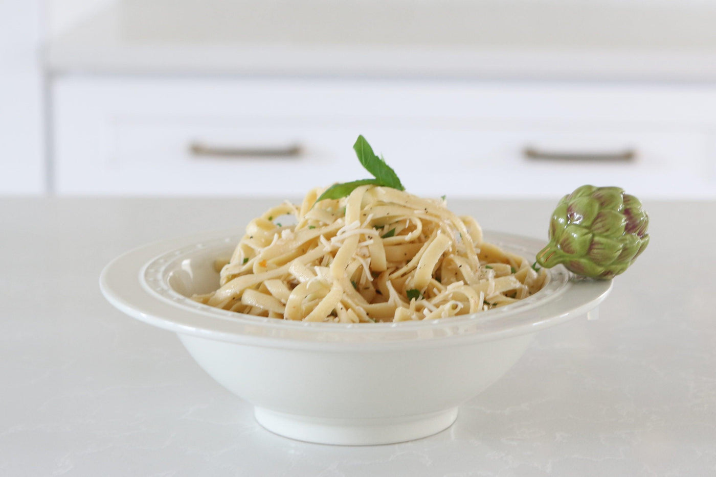 White stoneware bowl with pin dot design with noodles inside and an artichoke mini